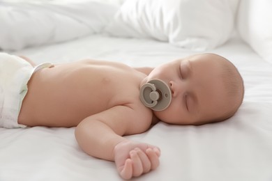 Cute little baby with pacifier sleeping on bed