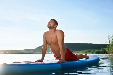 Photo of Man practicing yoga on light blue SUP board on river at sunset