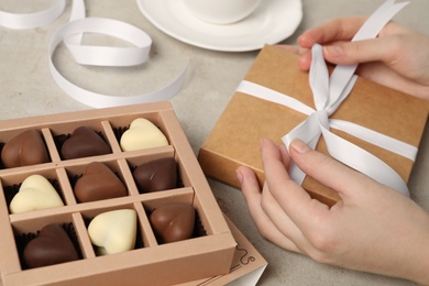 Woman with box of heart shaped chocolate candies at light table, closeup