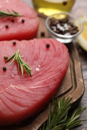 Photo of Raw tuna fillet with rosemary and peppercorns on board, closeup