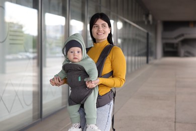 Mother holding her child in sling (baby carrier) near building outdoors