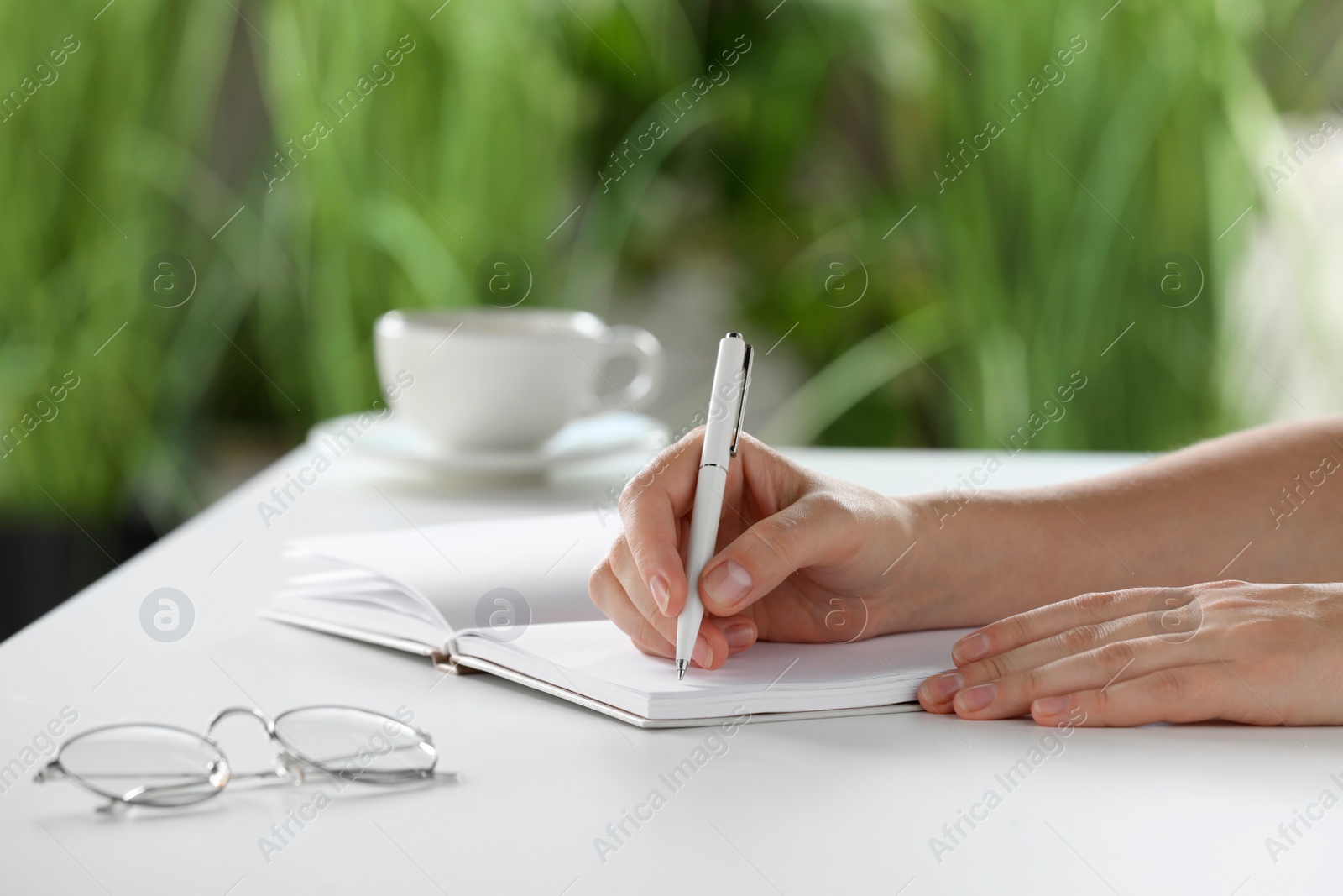 Photo of Woman writing in notebook at white table indoors, closeup