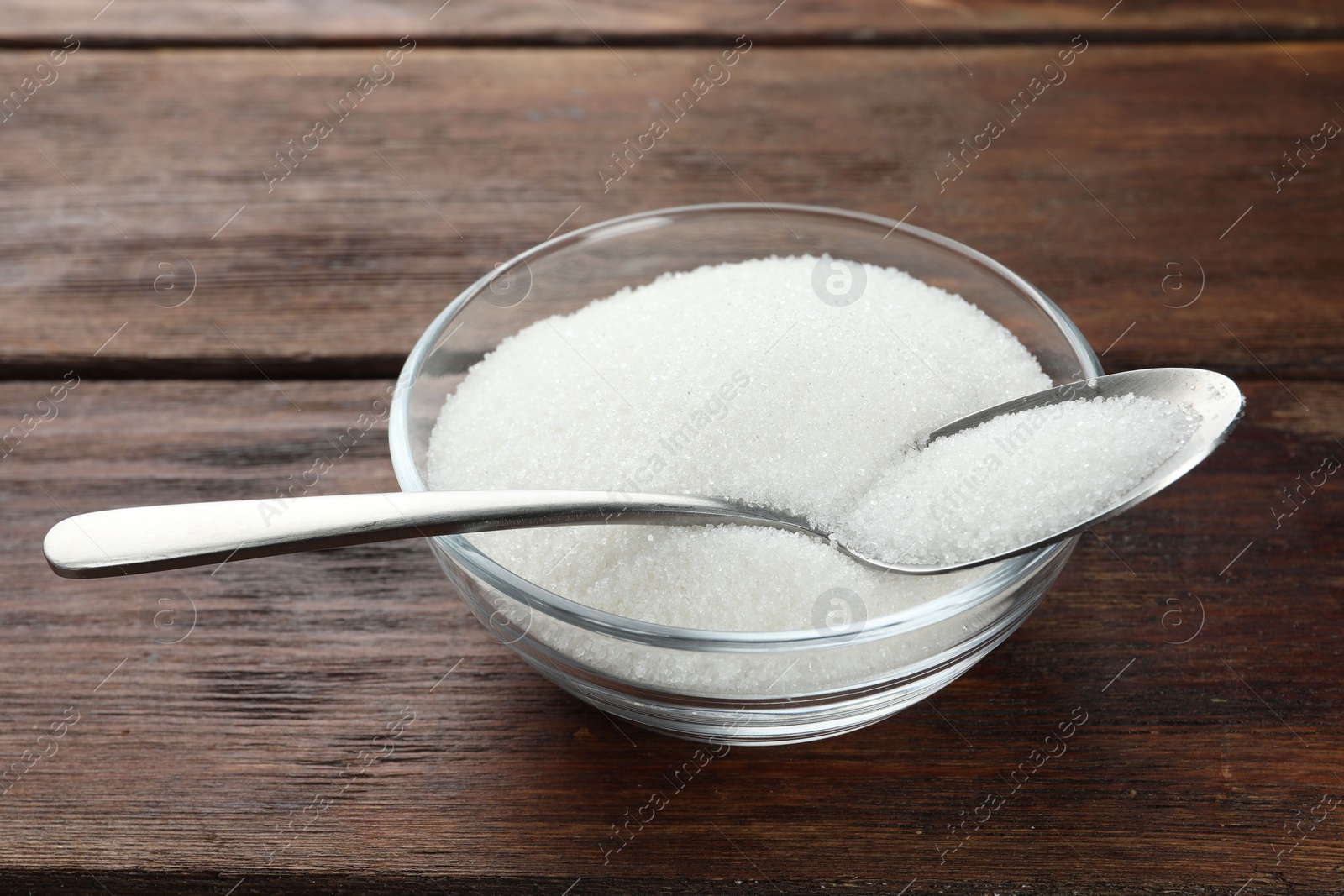 Photo of Granulated sugar in bowl and spoon on wooden table, closeup