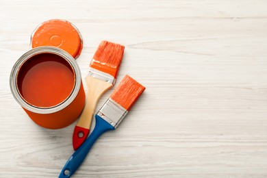 Photo of Can of orange paint and brushes on white wooden table, above view. Space for text