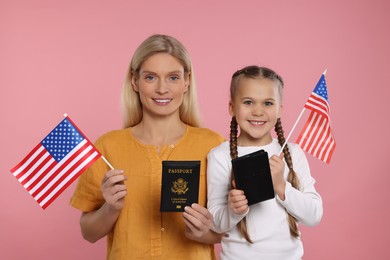 Immigration. Happy woman with her daughter holding passports and American flags on pink background