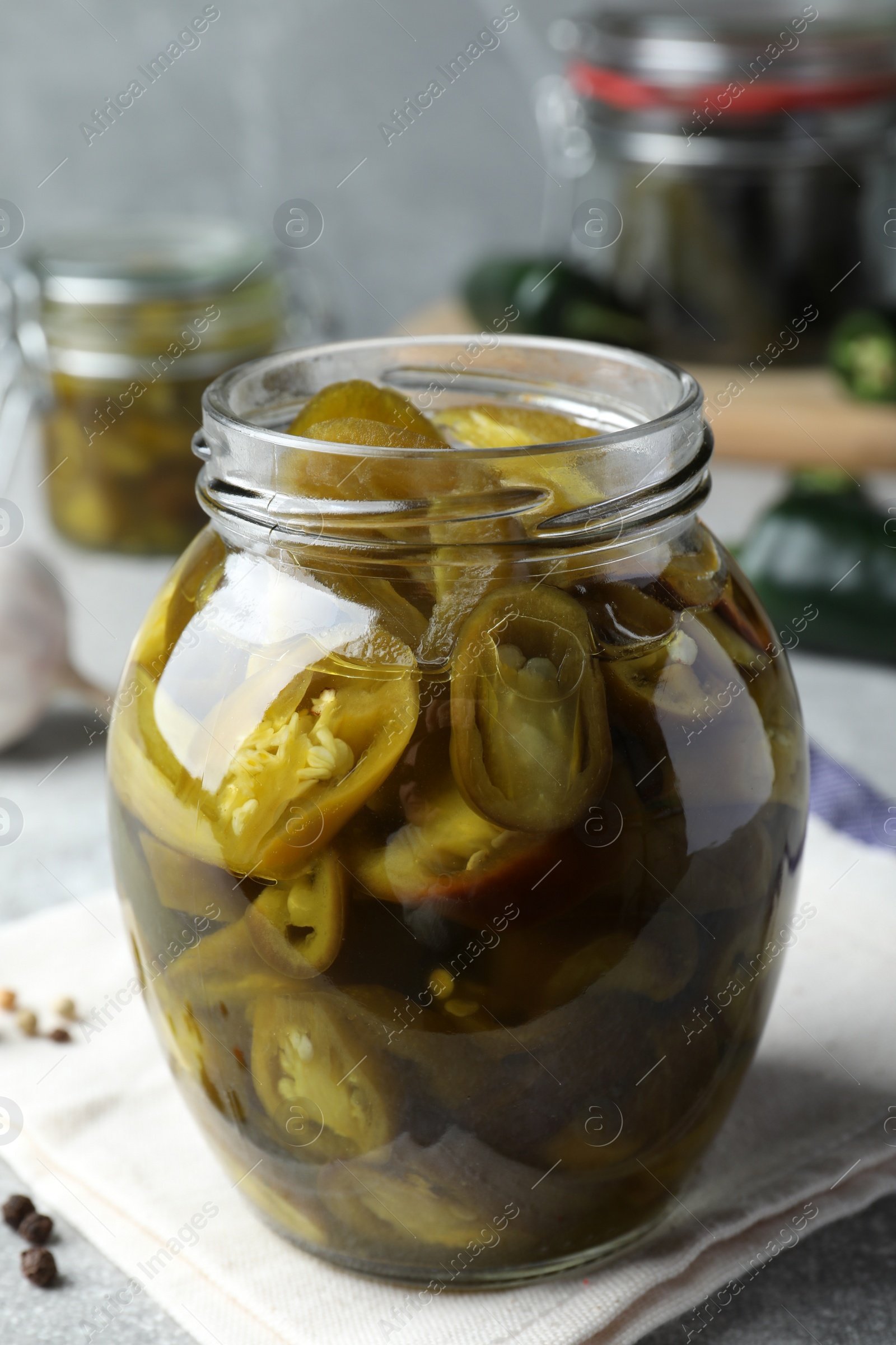 Photo of Glass jar with slices of pickled green jalapeno peppers on table
