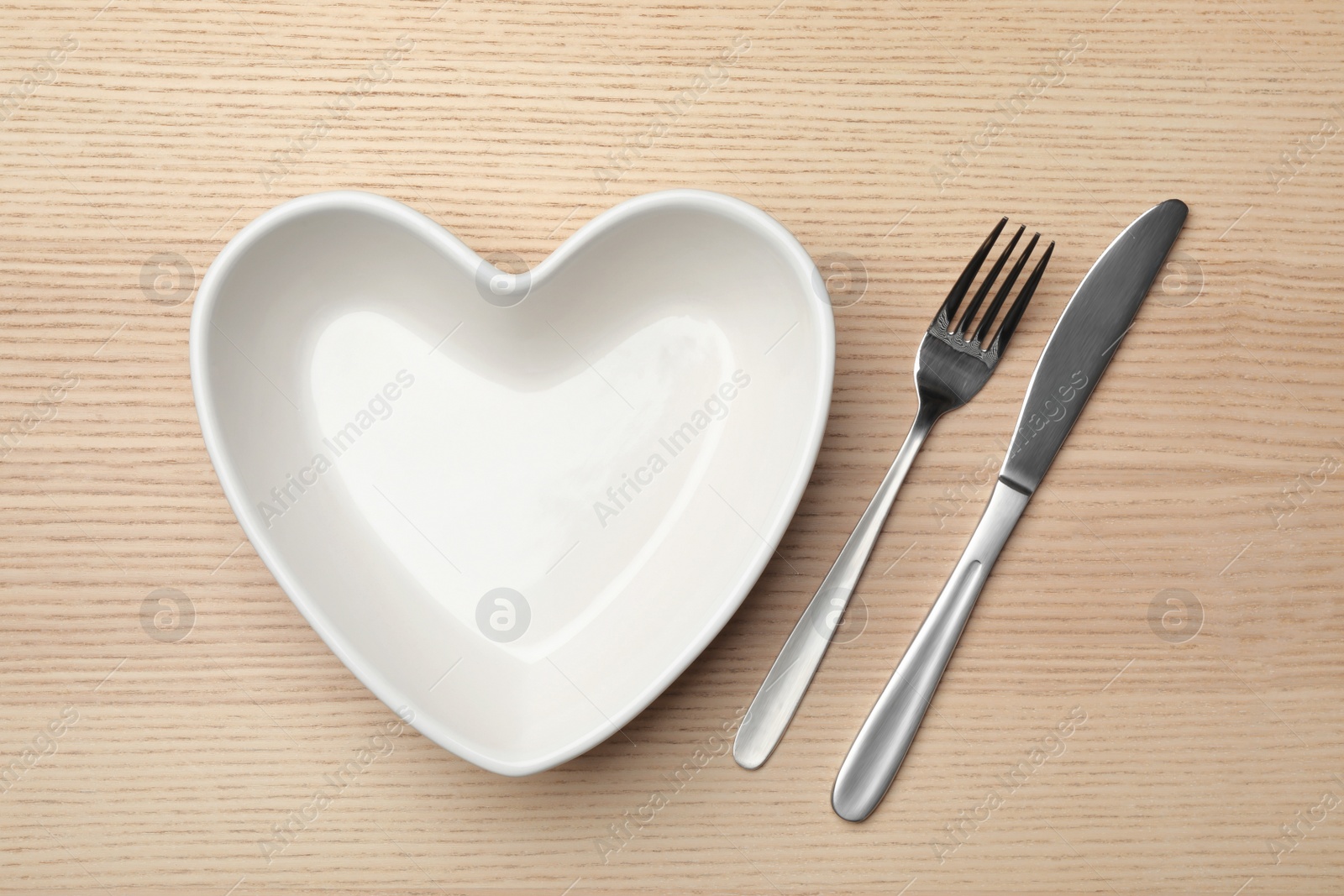 Photo of Heart shaped plate and cutlery on wooden background, flat lay