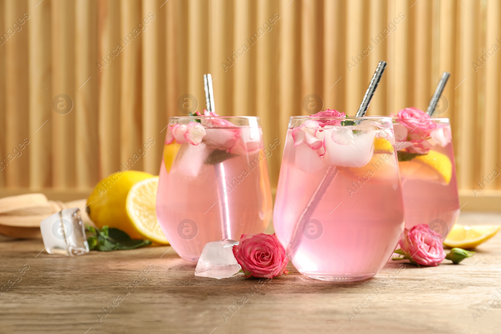 Photo of Delicious refreshing drink with rose flowers and lemon slices on wooden table