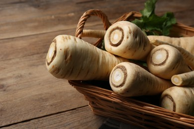 Photo of Wicker basket with delicious fresh ripe parsnips on wooden table, closeup