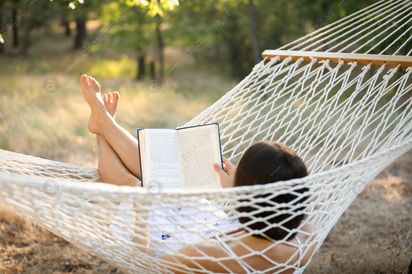 Photo of Young woman reading book in comfortable hammock at green garden