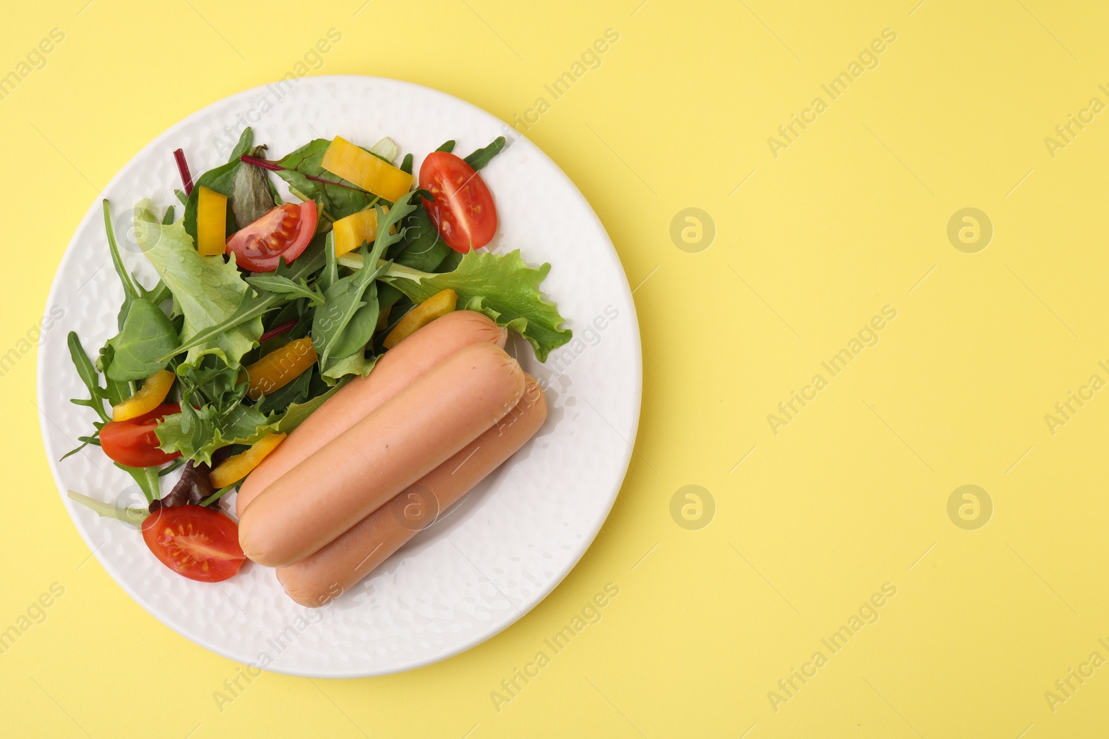 Photo of Delicious boiled sausages with salad on yellow background, top view. Space for text