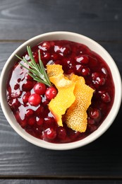Photo of Fresh cranberry sauce, rosemary and orange peel in bowl on black wooden table, top view