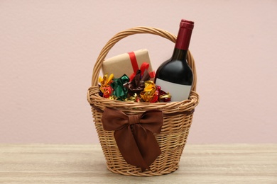 Photo of Wicker gift basket with food and wine on wooden table