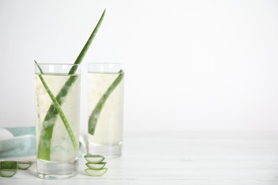 Photo of Fresh aloe drink with leaves in glasses on white wooden table. Space for text