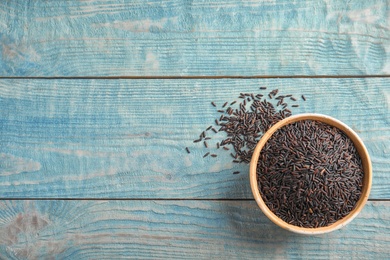 Bowl with uncooked black rice on blue wooden background, top view. Space for text