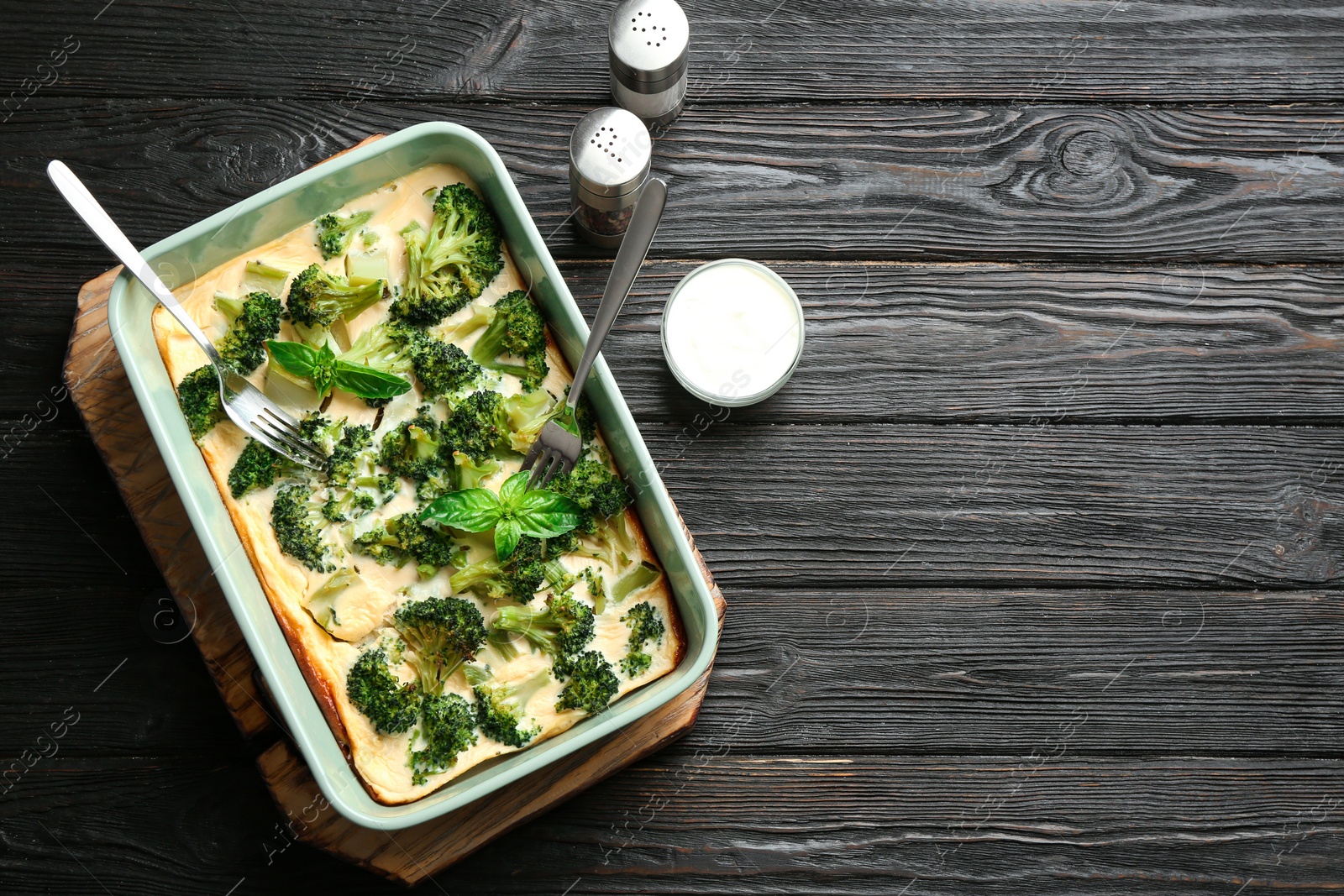 Photo of Tasty broccoli casserole in baking dish on black wooden table, flat lay. Space for text