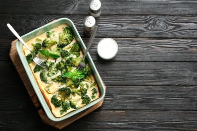 Photo of Tasty broccoli casserole in baking dish on black wooden table, flat lay. Space for text