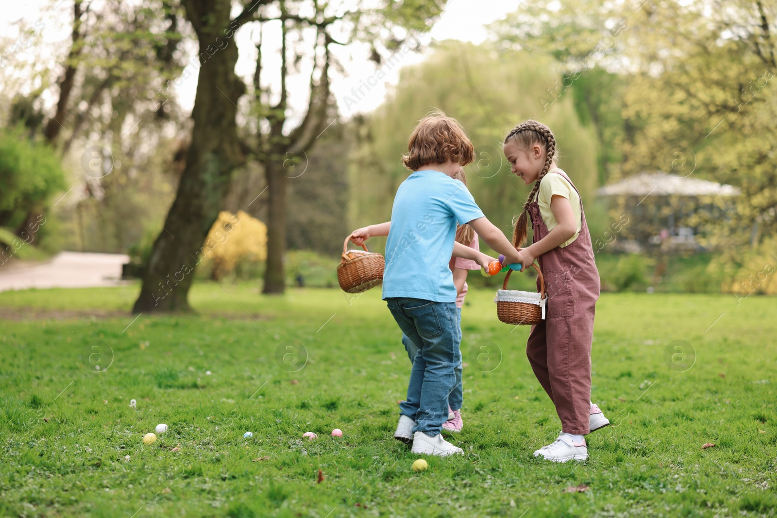 Photo of Easter celebration. Cute little children hunting eggs outdoors, space for text