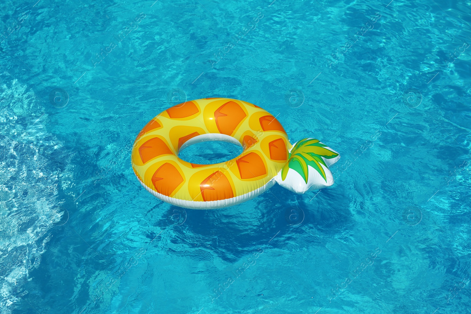 Photo of Bright inflatable pineapple ring floating in swimming pool on sunny day