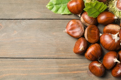 Photo of Fresh sweet edible chestnuts on wooden table, flat lay. Space for text