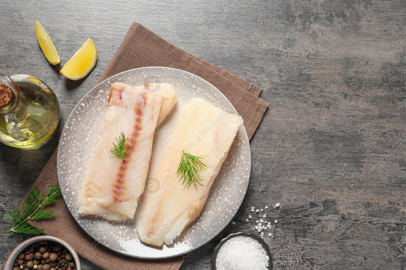 Photo of Pieces of raw cod fish, spices, oil and lemon on grey table, flat lay. Space for text