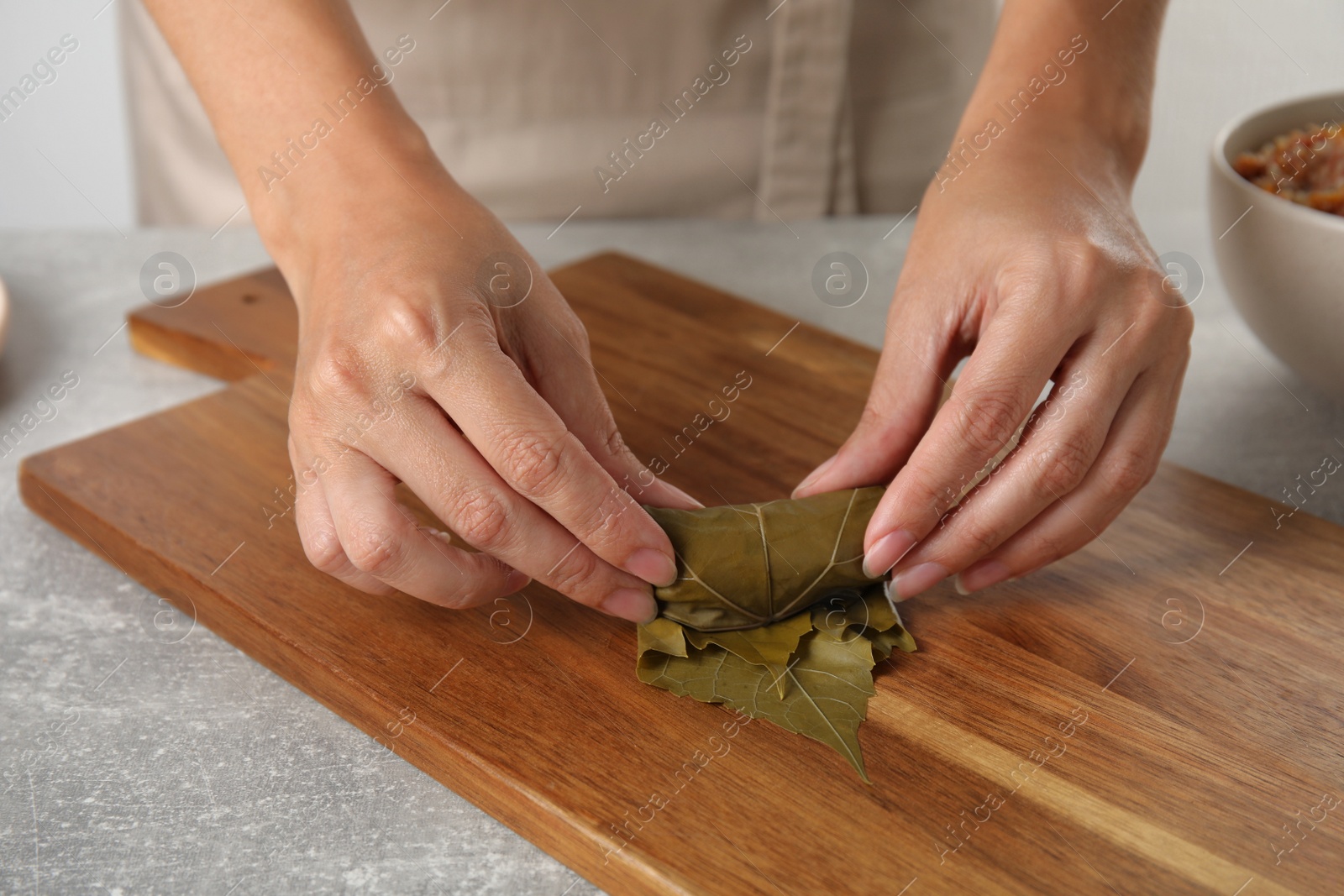 Photo of Woman preparing stuffed grape leaves at table, closeup