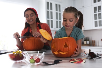 Photo of Mother and daughter making pumpkin jack o'lantern at table in kitchen. Halloween celebration