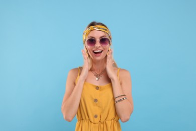 Photo of Portrait of surprised hippie woman in sunglasses on light blue background