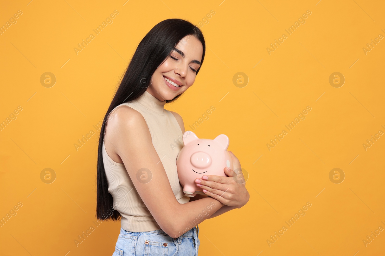 Photo of Happy young woman with piggy bank on orange background