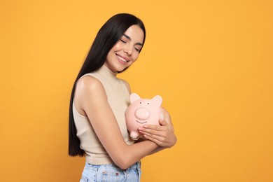 Happy young woman with piggy bank on orange background