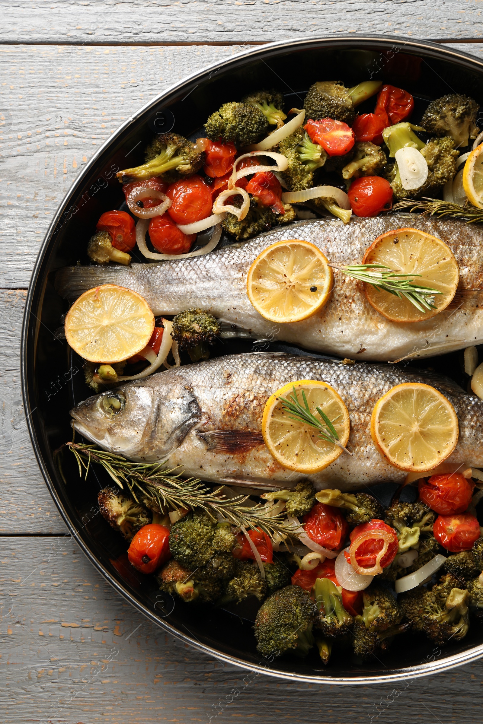 Photo of Baked fish with vegetables, rosemary and lemon on grey wooden table, top view