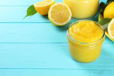 Photo of Delicious lemon curd in glass jar, fresh citrus fruits and green leaves on light blue wooden table, space for text