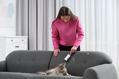Photo of Pet shedding. Woman with lint roller removing cat`s hair from sofa at home