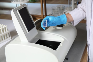 Scientist putting sample compartment with liquid in spectrophotometer, closeup. Laboratory analysis