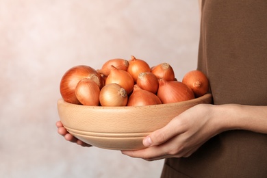 Woman holding bowl with ripe onions on grey background