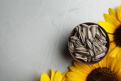 Photo of Raw sunflower seeds and flowers on grey table, flat lay. Space for text