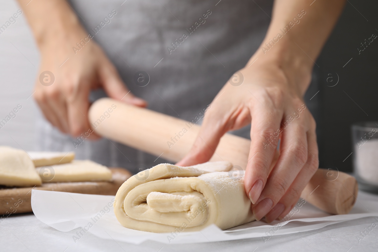 Photo of Woman with raw puff pastry dough at white table, closeup