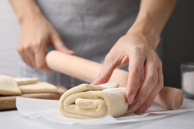 Photo of Woman with raw puff pastry dough at white table, closeup