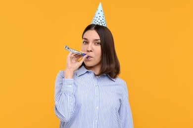 Photo of Young woman in party hat with blower on yellow background