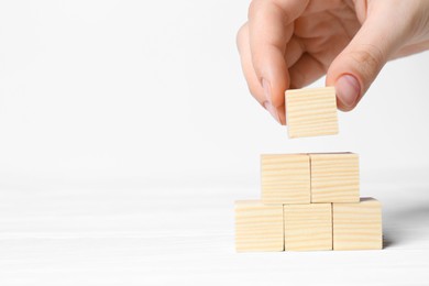 Photo of Woman building pyramid of cubes on white background, closeup with space for text. Idea concept