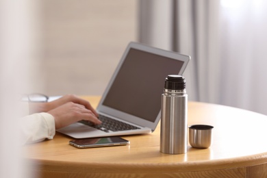 Photo of Woman with thermo bottle working at table in modern office, closeup
