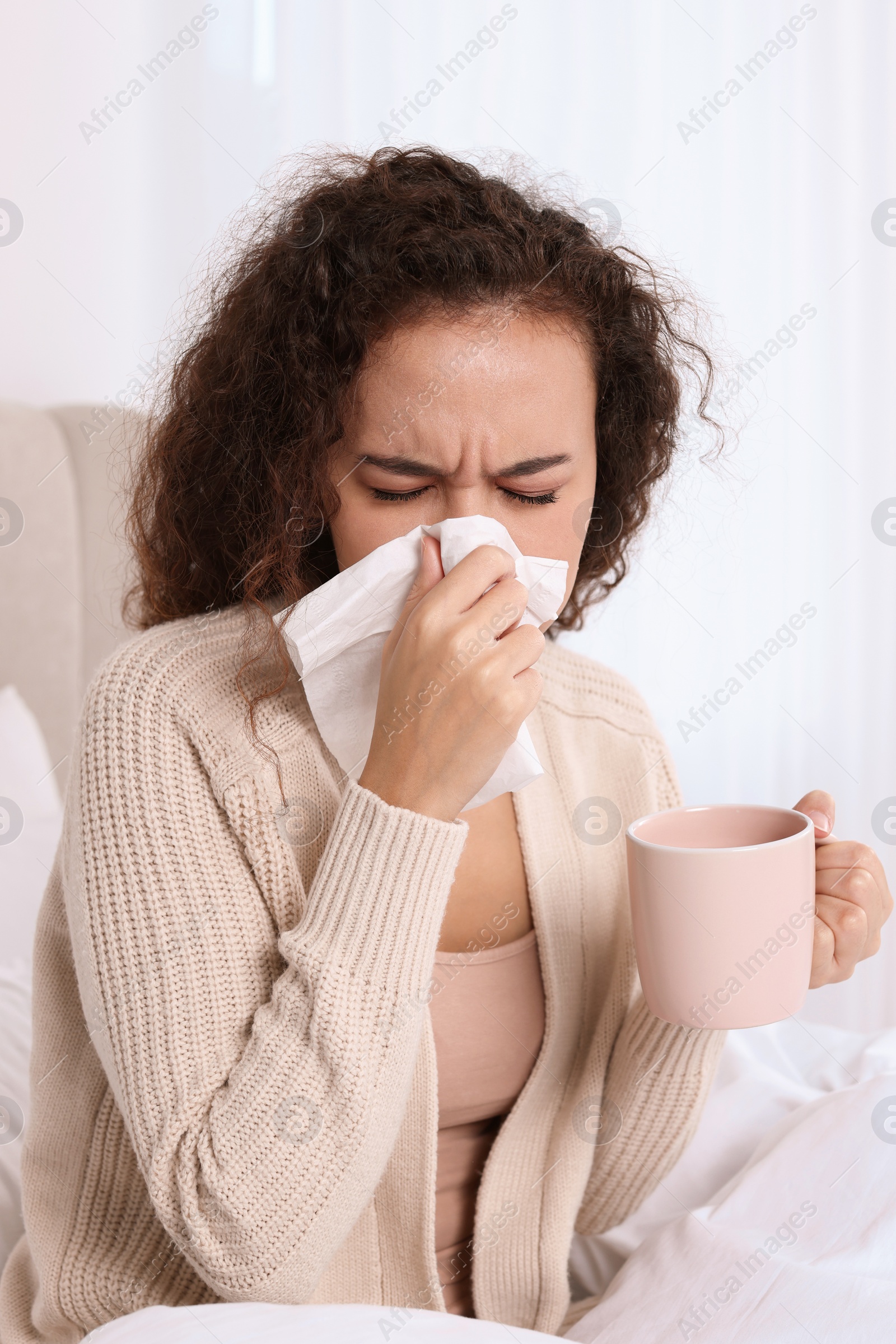 Photo of Sick African American woman with tissue and cup of drink in bed at home