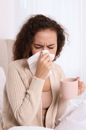 Sick African American woman with tissue and cup of drink in bed at home