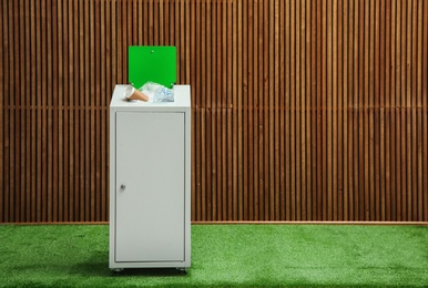 Overfilled trash bin near wooden wall indoors, space for text. Recycling concept