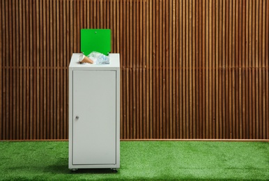 Photo of Overfilled trash bin near wooden wall indoors, space for text. Recycling concept