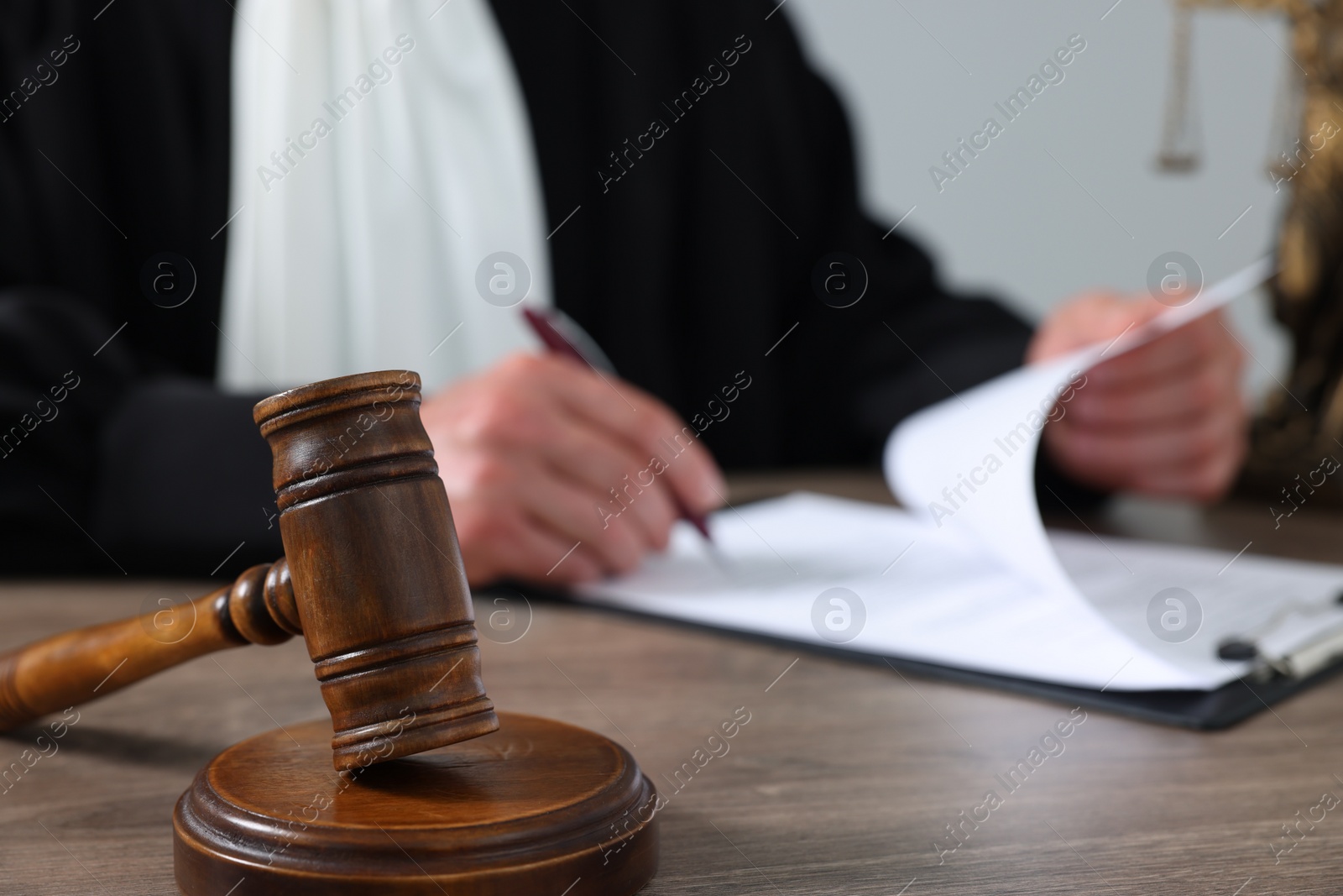 Photo of Judge with gavel writing in papers at wooden table against light grey background, closeup