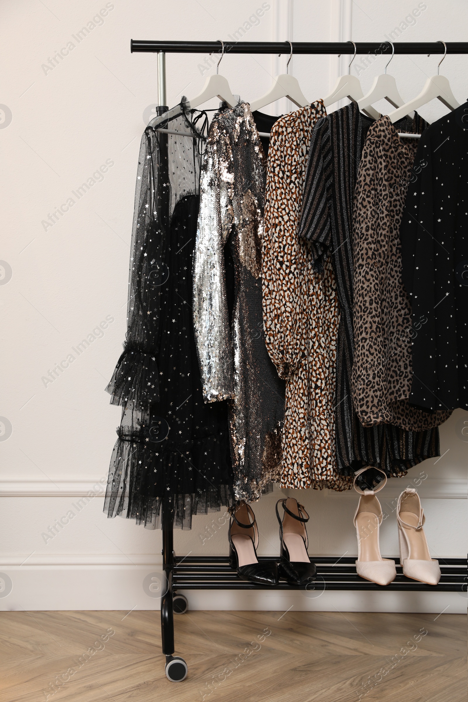 Photo of Storage rack with stylish clothes and shoes near white wall. Dressing room interior