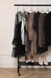 Photo of Storage rack with stylish clothes and shoes near white wall. Dressing room interior