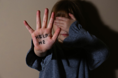 Crying little girl showing palm with phrase HELP ME near beige wall, focus on hand. Domestic violence concept