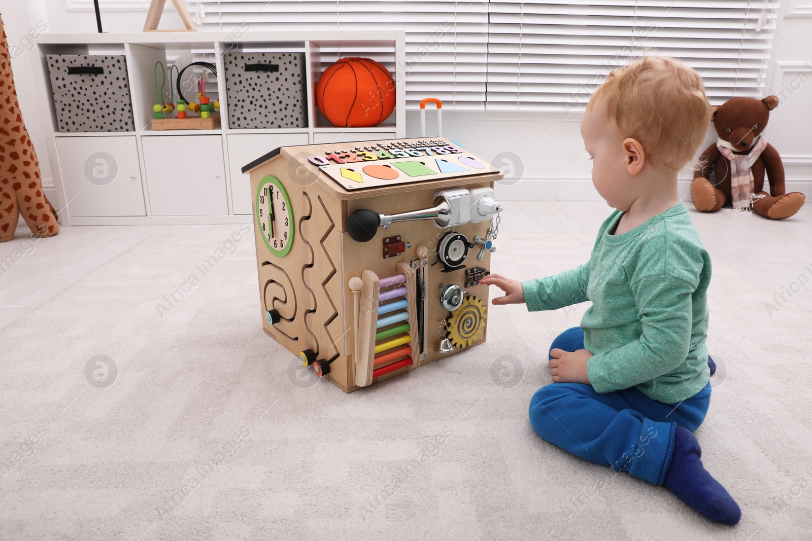 Photo of Cute little boy playing with busy board house on floor at home